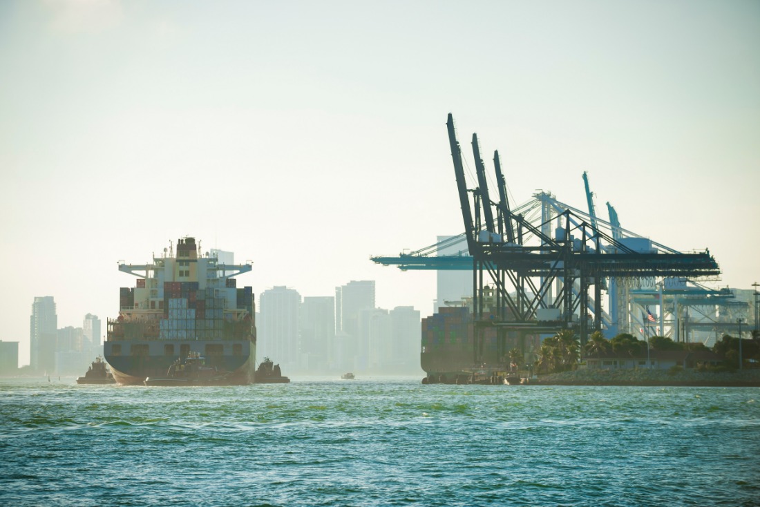 Container ship approaching port with cranes and city skyline in the background